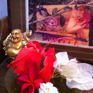 Rote Hibiskus-Blüte, goldener Buddha, weiße Bougainvillea und ein Foto im Hintergrund mit Kristallkugel und Lilie